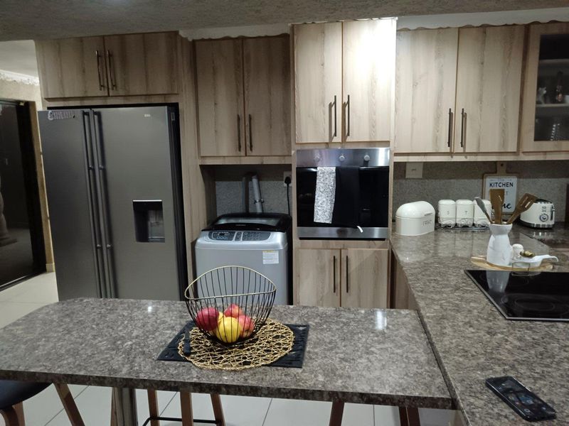 Modern kitchen featuring light wood-grain cabinetry, stone-look countertops, built-in oven, and electric cooktop with a functional breakfast bar layout.