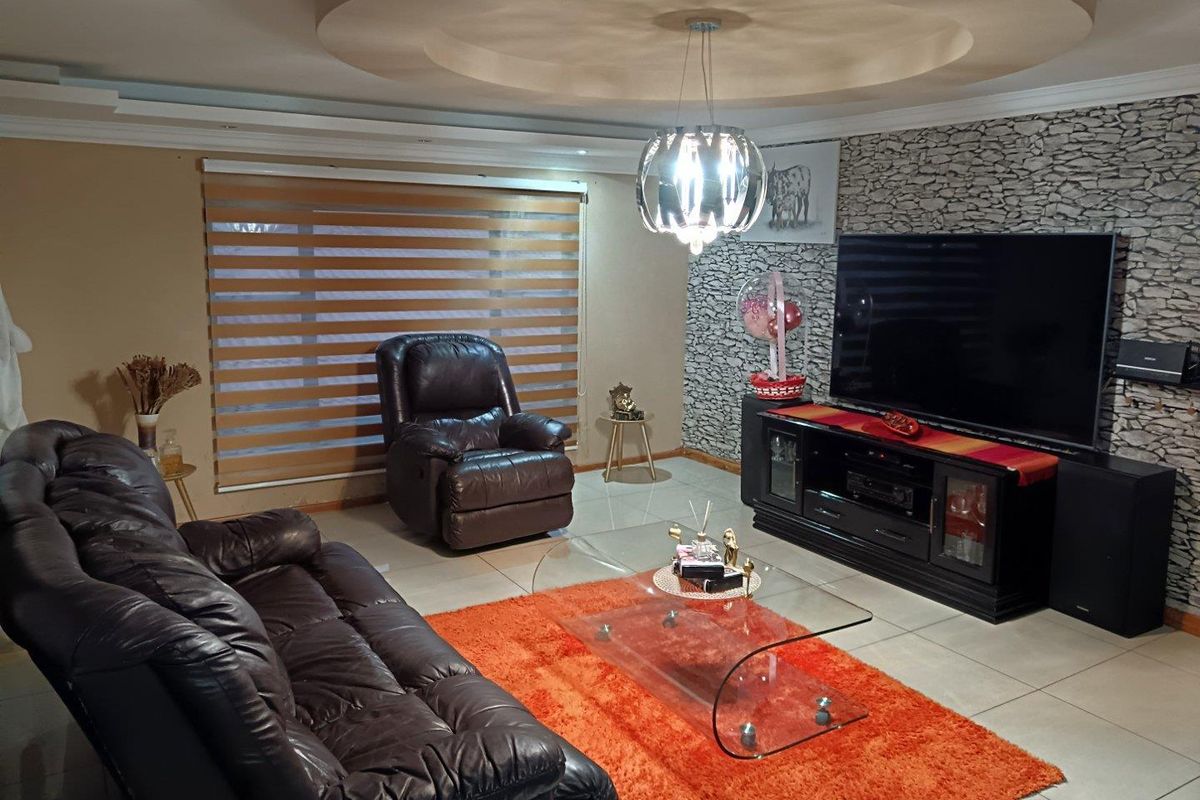 A comfortable living room featuring a stone-cladding accent wall, recessed ceiling detail, and neutral tiled flooring.
