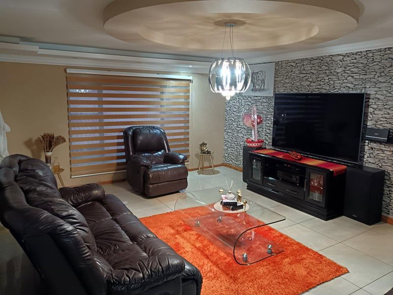 A comfortable living room featuring a stone-cladding accent wall, recessed ceiling detail, and neutral tiled flooring.