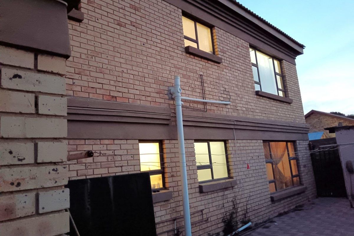 Rear exterior view of a double-storey face brick house featuring aluminium window frames and a paved patio area.