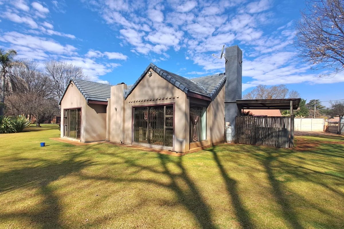 Rear view of a residential house featuring a tiled roof, brick chimney, and sliding glass doors leading to a garden area.