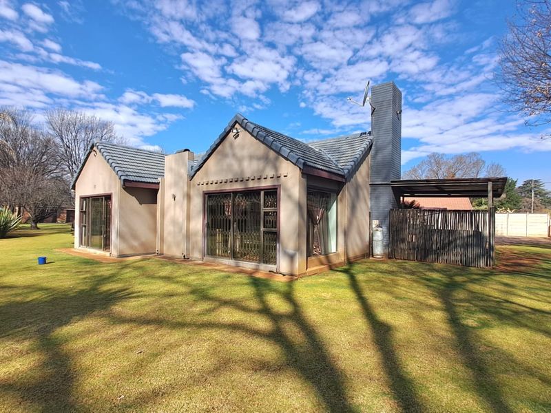 Rear view of a residential house featuring a tiled roof, brick chimney, and sliding glass doors leading to a garden area.