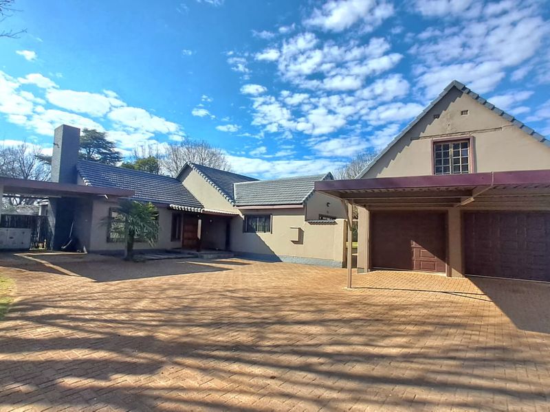 Front view of a residential property featuring a large paved driveway, double garage, attached carport, and a tiled roof structure.