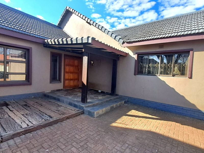 Front entrance of the house featuring a covered porch, timber front door, paved driveway, and decorative timber sleeper decking.