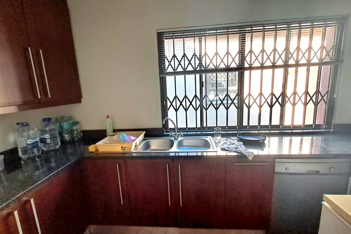A functional kitchen featuring dark laminate cabinetry, granite countertops, a double bowl sink, and a security gate over the window.