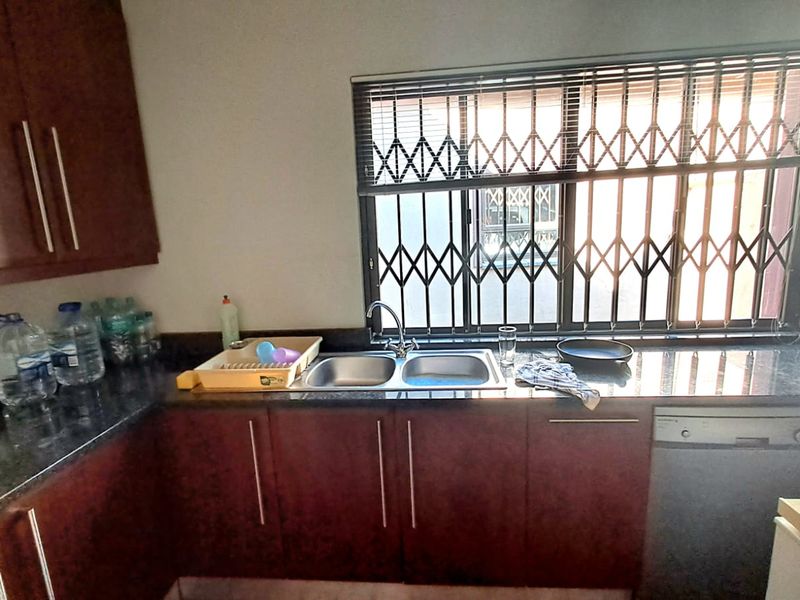 A functional kitchen featuring dark laminate cabinetry, granite countertops, a double bowl sink, and a security gate over the window.