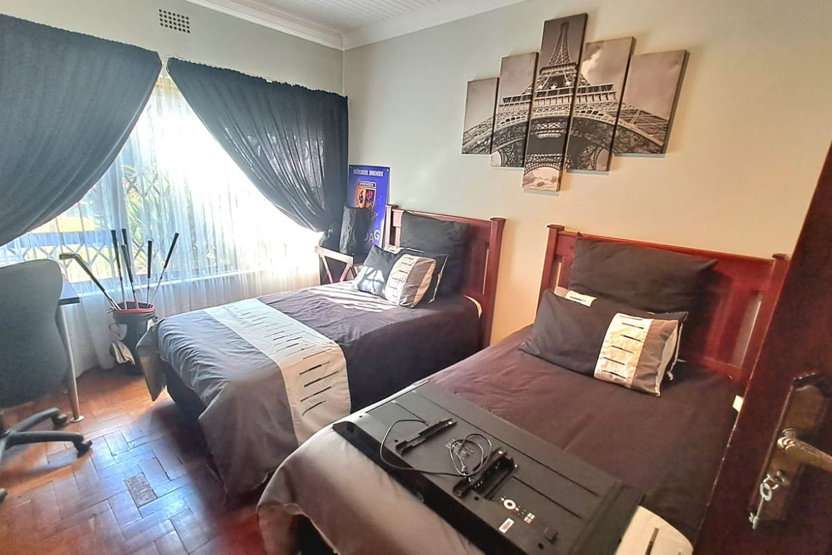 A bedroom featuring parquet flooring and classic cornicing, currently configured with twin beds and natural light from a large sliding window.