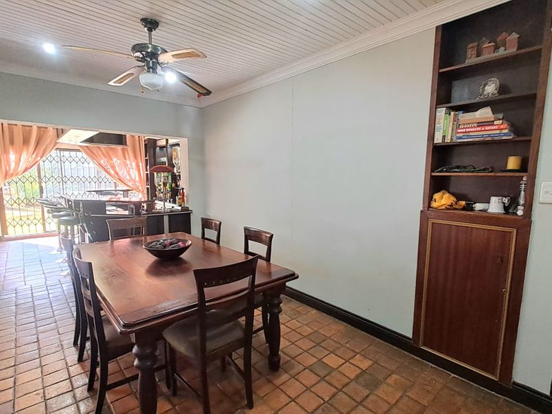 Dining area featuring terracotta floor tiles, a tongue and groove ceiling, and built-in wooden shelving, with an open-plan flow to the adjacent living space.