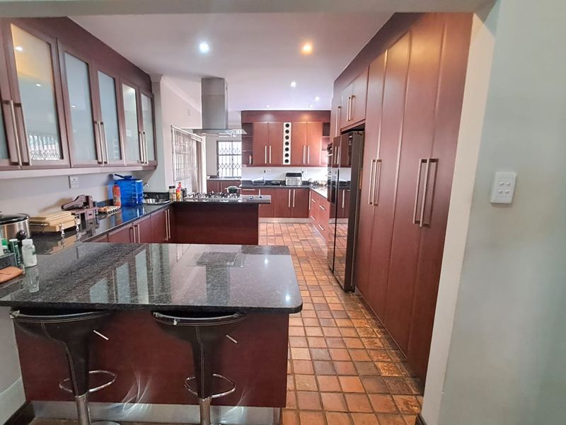 Spacious kitchen featuring dark wood cabinetry, granite countertops, integrated appliances, and tiled flooring with a breakfast bar area.