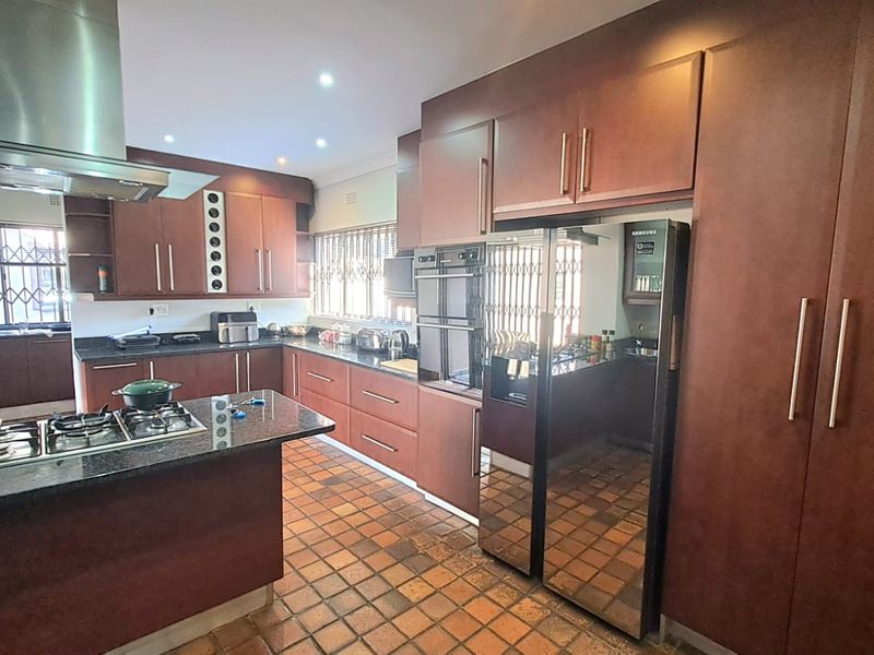 Spacious kitchen featuring dark wood cabinetry, granite countertops, a gas hob with stainless steel extractor, and durable terracotta tile flooring.