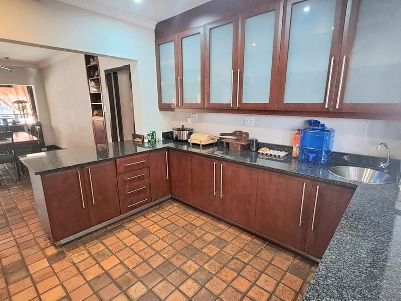 A functional kitchen featuring dark wood cabinetry, granite countertops, a gas hob, and terracotta floor tiles, with an open-plan layout connecting to the dining area.
