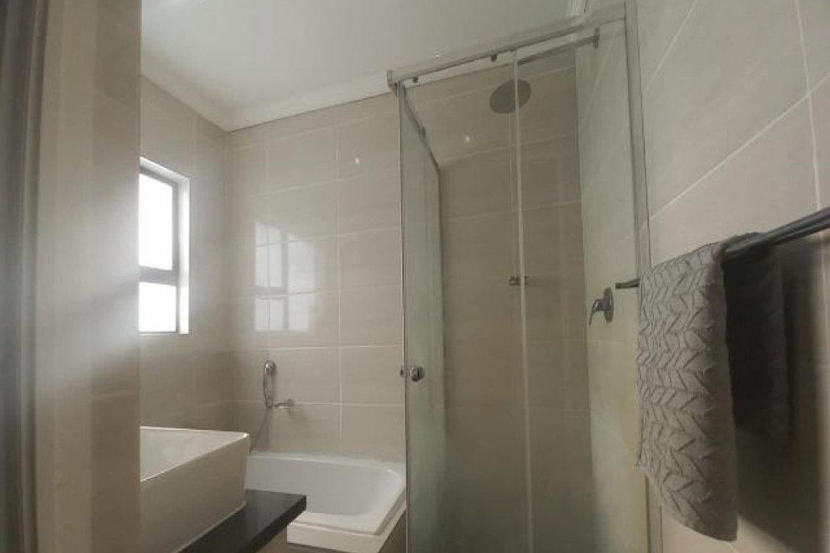 Modern bathroom featuring a glass-enclosed shower, a built-in bathtub, and neutral wall tiling.