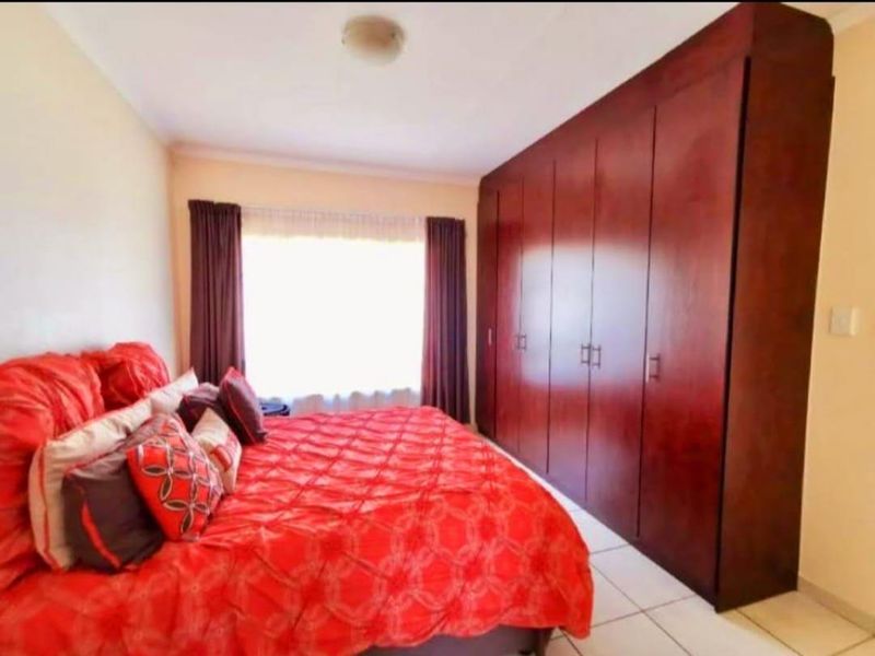 A bedroom featuring large dark wood built-in cupboards and tiled flooring.