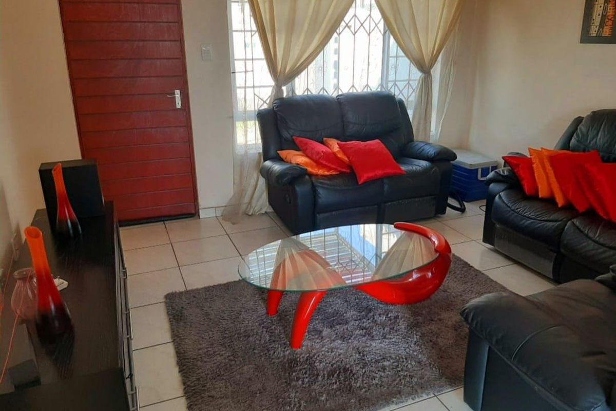 A living room featuring tiled flooring, a window with security bars, and a solid red door.