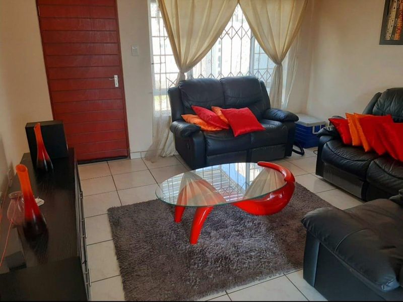 A living room featuring tiled flooring, a window with security bars, and a solid red door.