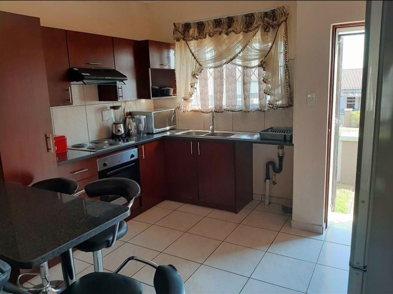 A functional kitchen featuring dark wood cabinetry, granite-look countertops, built-in oven and hob, and direct access to the exterior.