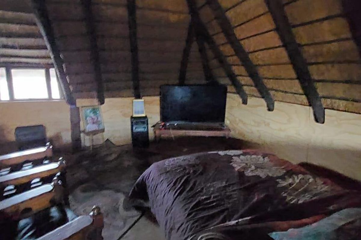 Attic-style bedroom featuring exposed timber roof beams, a thatched ceiling, and plywood wall paneling in a rustic farm-style setting.