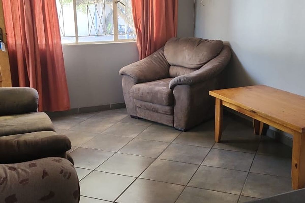 A living room area featuring tiled flooring, a large window with curtain tracks, and wall-mounted television bracket with exposed cabling.