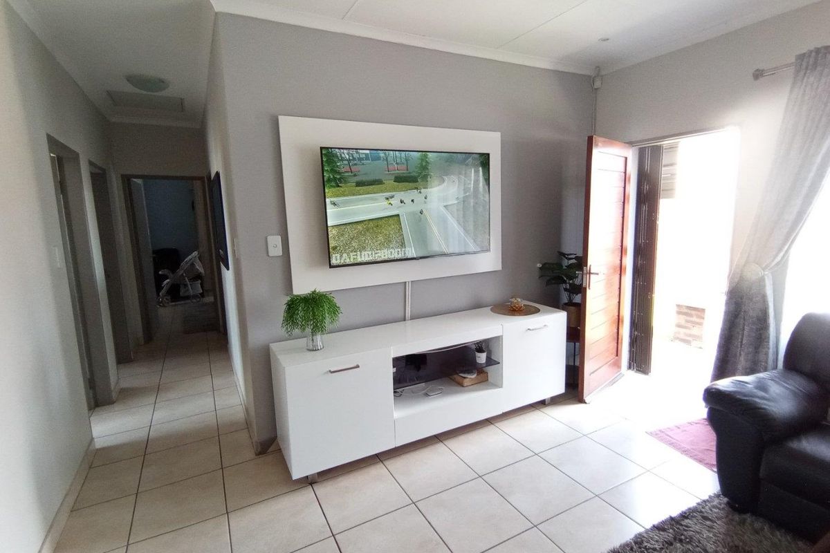 A living room area featuring tiled flooring, a wall-mounted television unit, and direct access to an outdoor space through a wooden door.