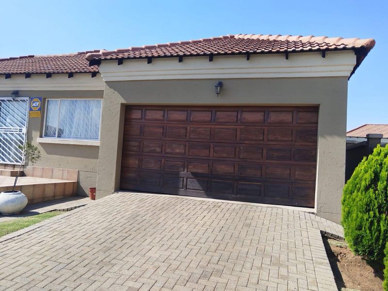 Front elevation of the property featuring a paved driveway, a wooden sectional garage door, and secure window treatments.