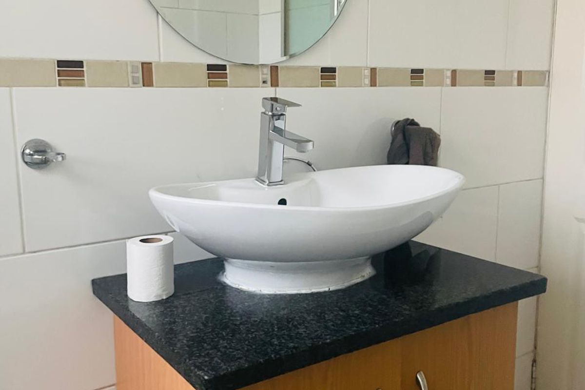 A functional bathroom vanity featuring a modern vessel sink, granite countertop, and wood-finish cabinetry with chrome hardware.