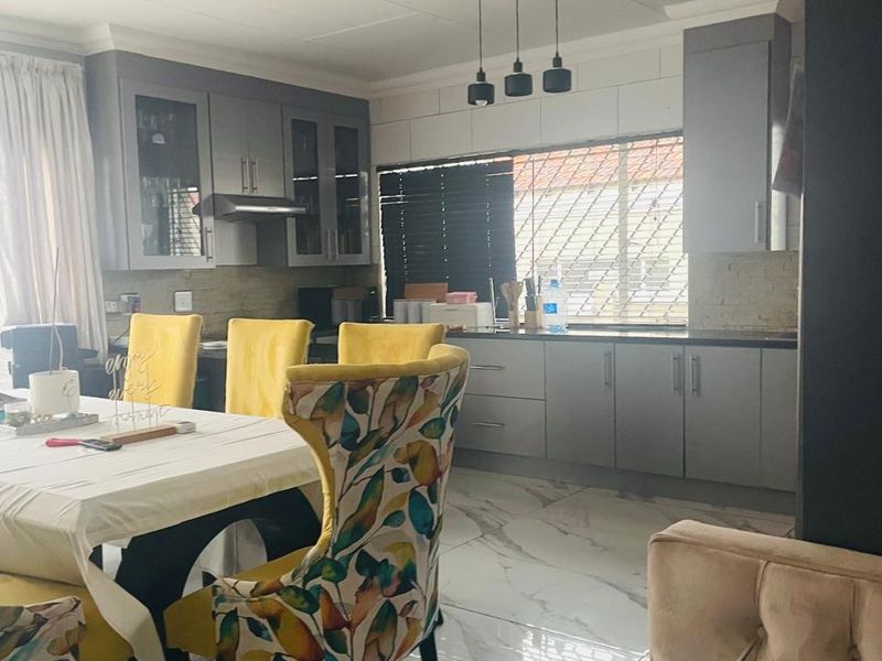 Open plan kitchen and dining area featuring modern grey cabinetry, stone tile flooring, and contemporary pendant lighting.