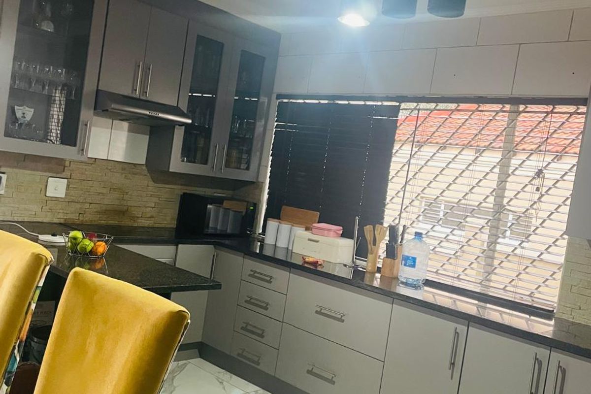 Modern kitchen featuring sleek grey cabinetry, granite countertops, stone tile backsplash, and elegant marble-look floor tiles with contemporary pendant lighting.