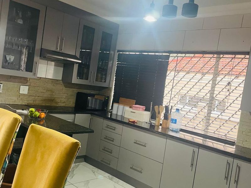 Modern kitchen featuring sleek grey cabinetry, granite countertops, stone tile backsplash, and elegant marble-look floor tiles with contemporary pendant lighting.