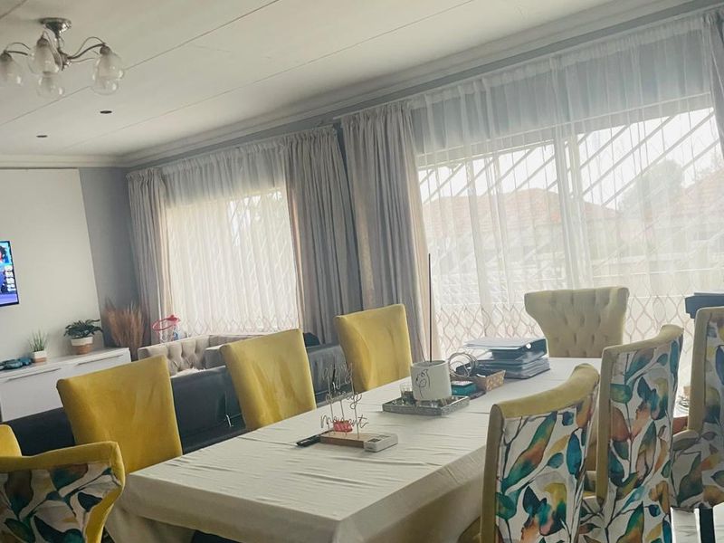 A bright dining room featuring tiled flooring, recessed lighting, and large windows fitted with security gates and curtains.
