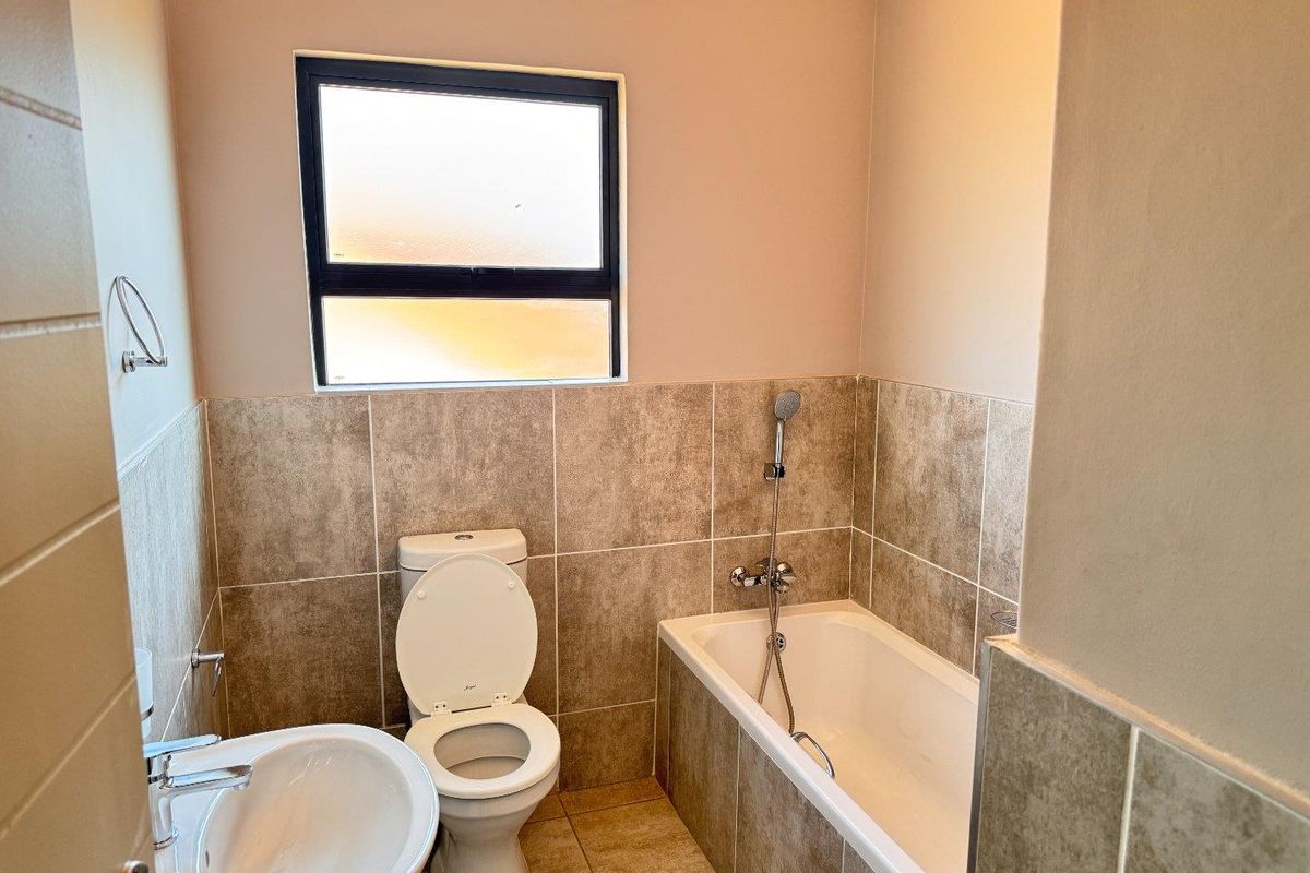 A functional bathroom featuring a bathtub with a handheld shower attachment, a toilet, and a pedestal basin with tiled walls and flooring.
