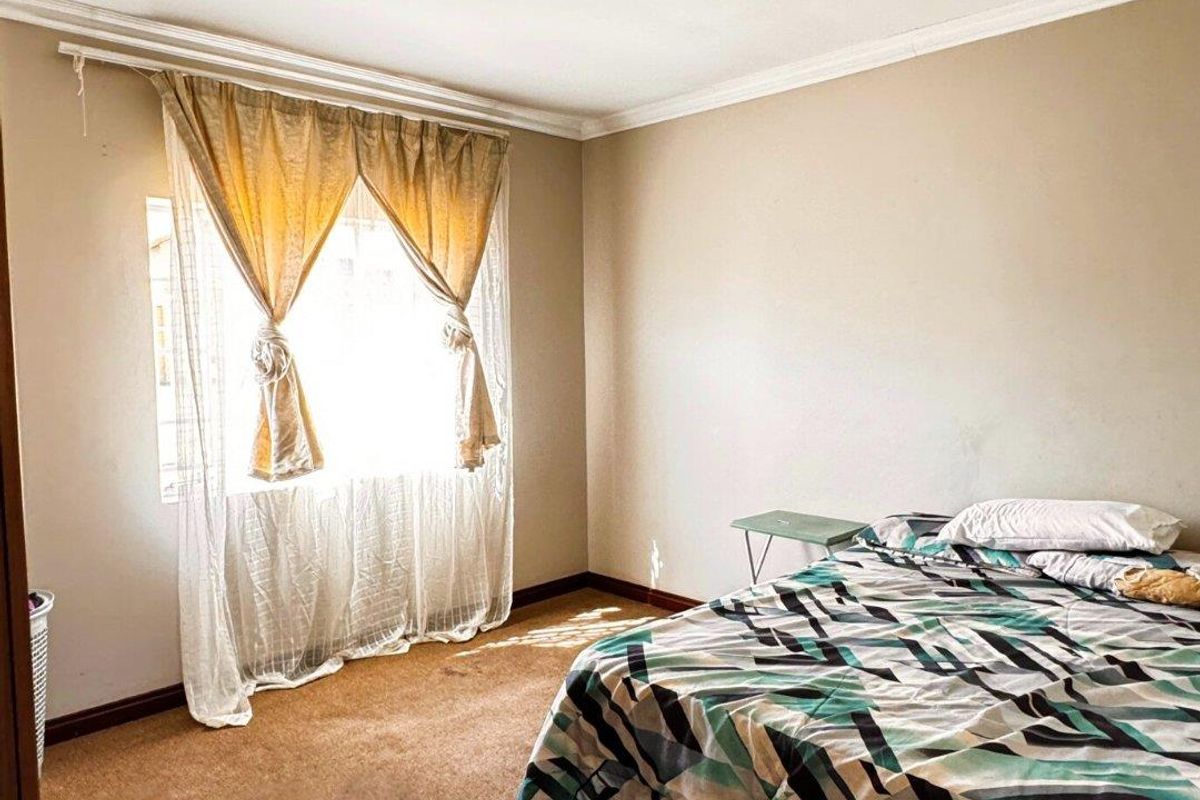 A bedroom featuring carpeted flooring, a window with curtains, and a central ceiling light fixture.