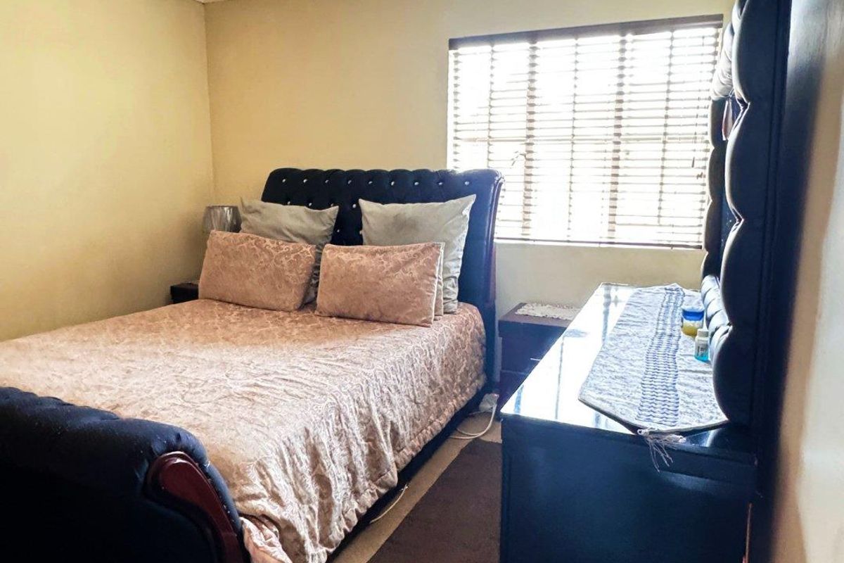 A standard bedroom featuring carpeted flooring, a window with fitted blinds, and a central ceiling light fixture.