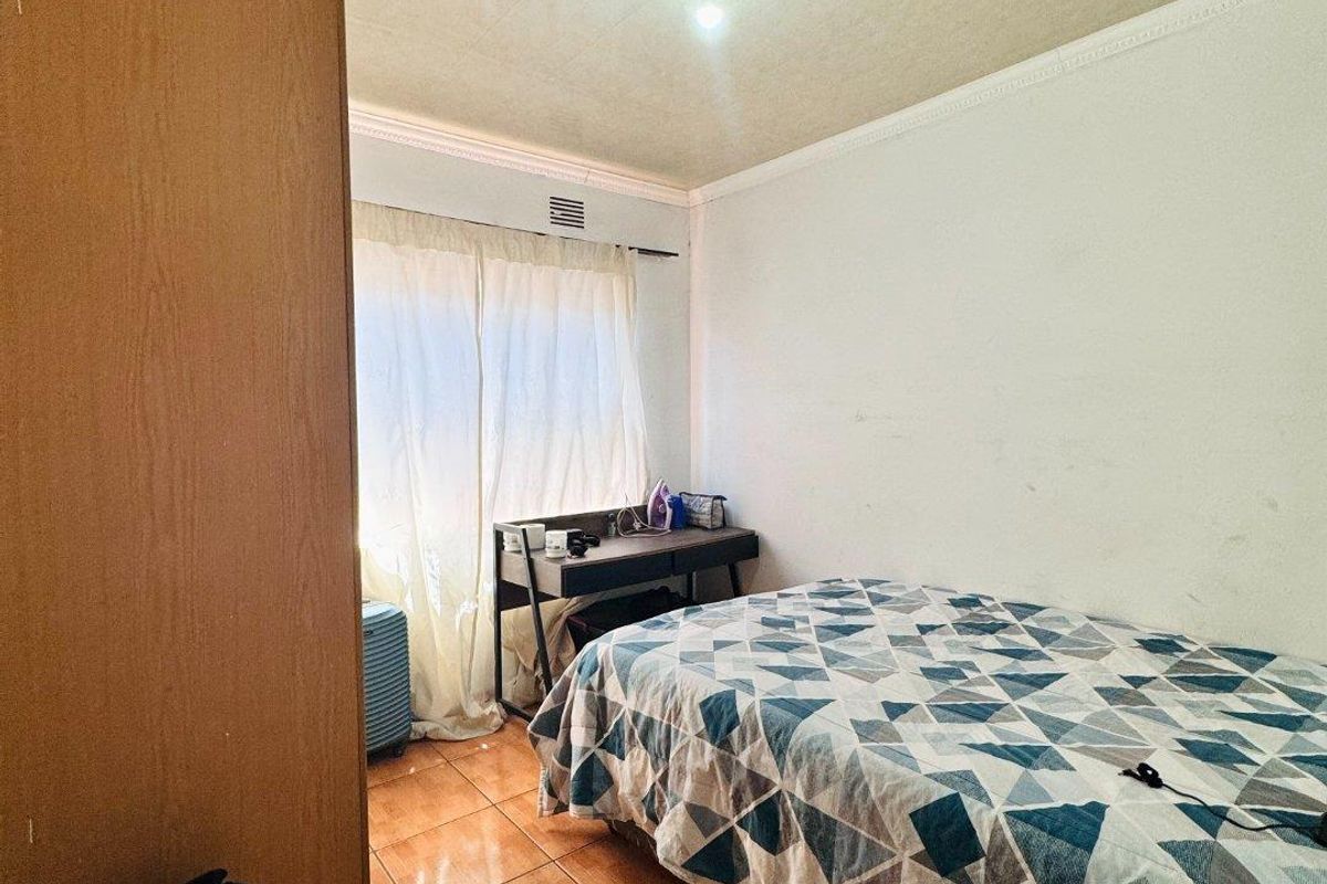 A functional bedroom featuring tiled flooring, built-in cabinetry, and a window with curtaining, providing a simple and practical living space.