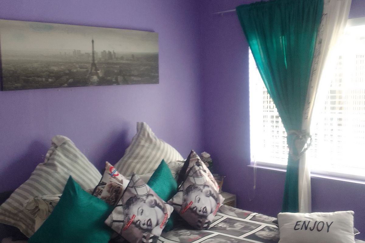 A bedroom featuring a ceiling fan and window blinds, currently decorated with vibrant purple walls.