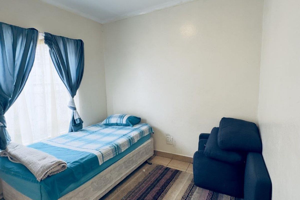 A compact bedroom featuring tiled flooring and a single window with curtain fixtures.
