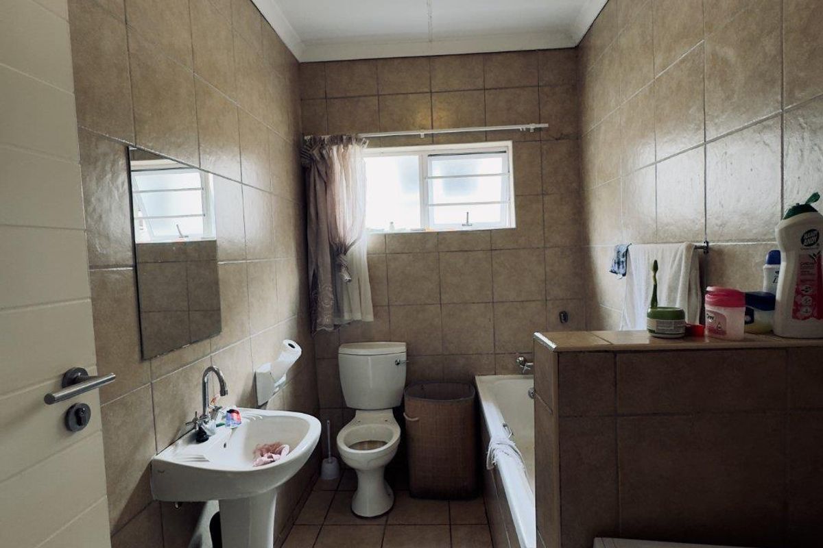 A functional bathroom featuring a pedestal basin, toilet, and a tiled bathtub enclosure with neutral wall and floor tiling.