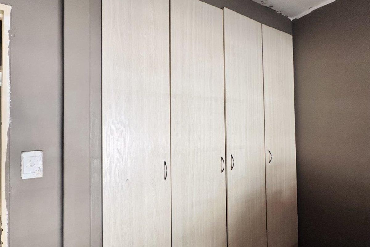 A bedroom featuring built-in light wood-toned cabinetry with vertical handles, set against dark grey walls.