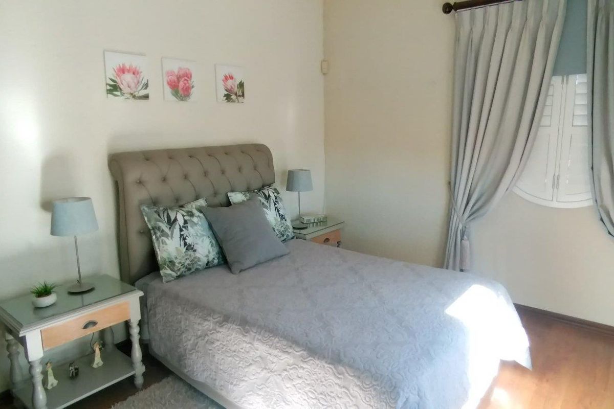 A well-lit bedroom featuring wooden flooring, neutral wall tones, and classic window treatments, providing a comfortable and functional living space.