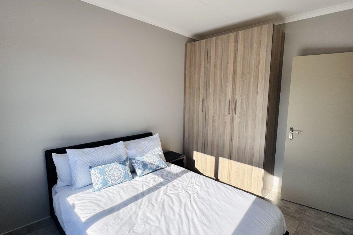 A well-lit bedroom featuring neutral wall tones, tiled flooring, and a built-in wooden wardrobe.