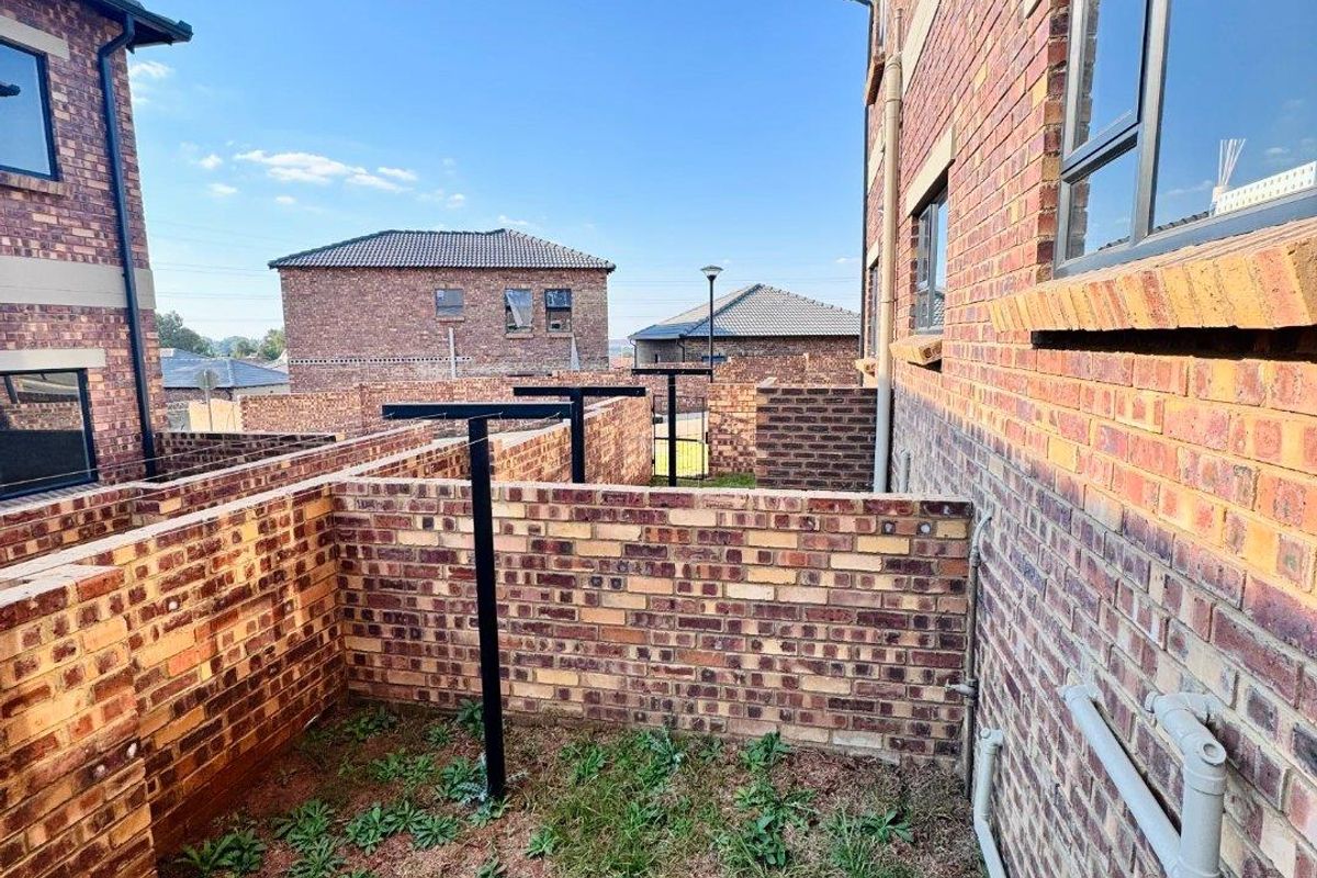 A side exterior view of the property featuring face-brick walls, a small garden area with a washing line, and external plumbing fixtures.