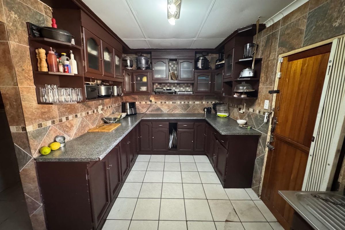 A dated kitchen featuring dark wood cabinetry, granite countertops, and tiled splashbacks, offering a functional layout with potential for modern renovation.