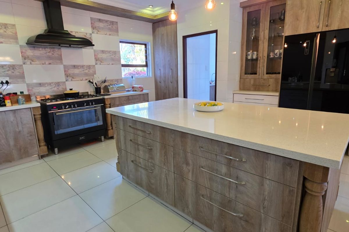 Modern kitchen featuring a large central island with stone countertops, wood-grain cabinetry, a gas stove with extractor fan, and tiled flooring.