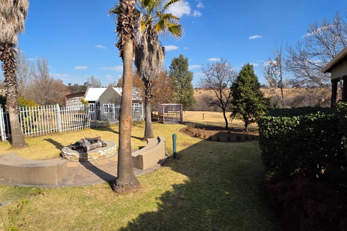 Spacious rear garden featuring a built-in stone fire pit with curved concrete seating, mature palm trees, and a fenced perimeter overlooking open fields.