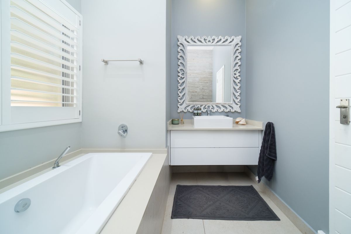 A modern bathroom featuring a built-in bathtub, a wall-mounted vanity with a vessel sink, and plantation shutters.