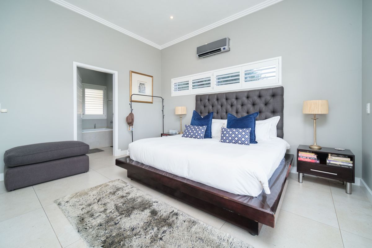Spacious bedroom featuring neutral walls, tiled flooring, crown molding, and a wall-mounted air conditioning unit, with an adjoining en-suite bathroom.