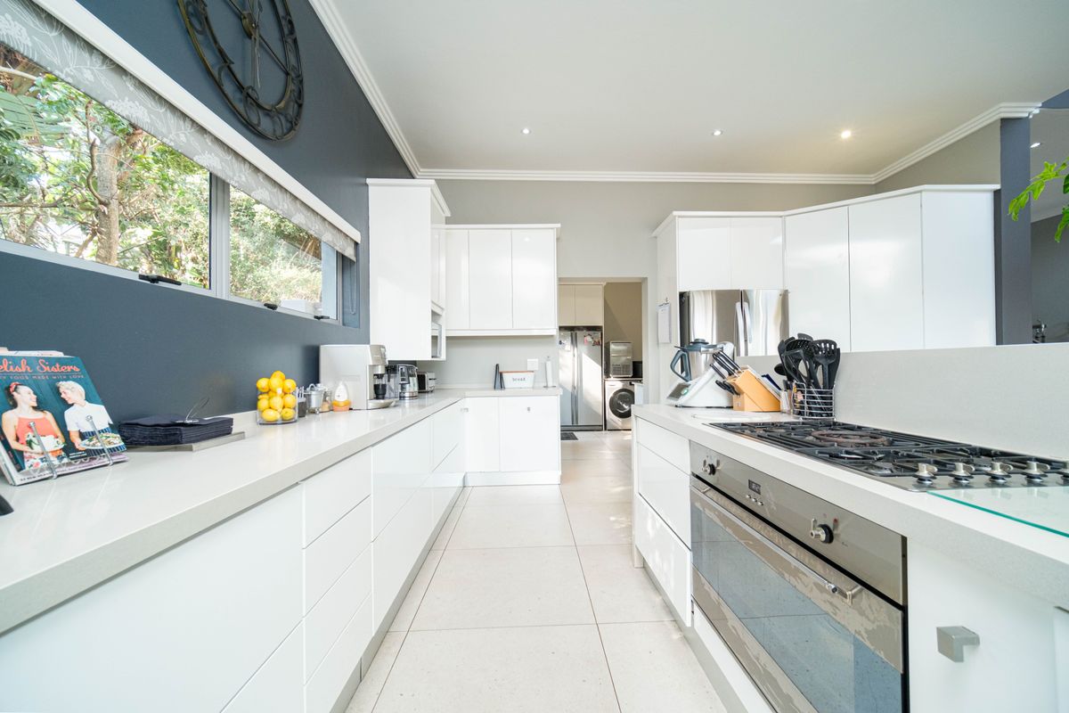 Modern kitchen featuring sleek white cabinetry, stone countertops, a built-in gas hob, and an integrated oven, with a seamless transition to a laundry area.