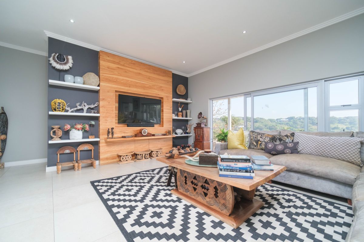 A bright and modern living room featuring a custom wood-paneled media wall with built-in shelving and large windows offering scenic views.