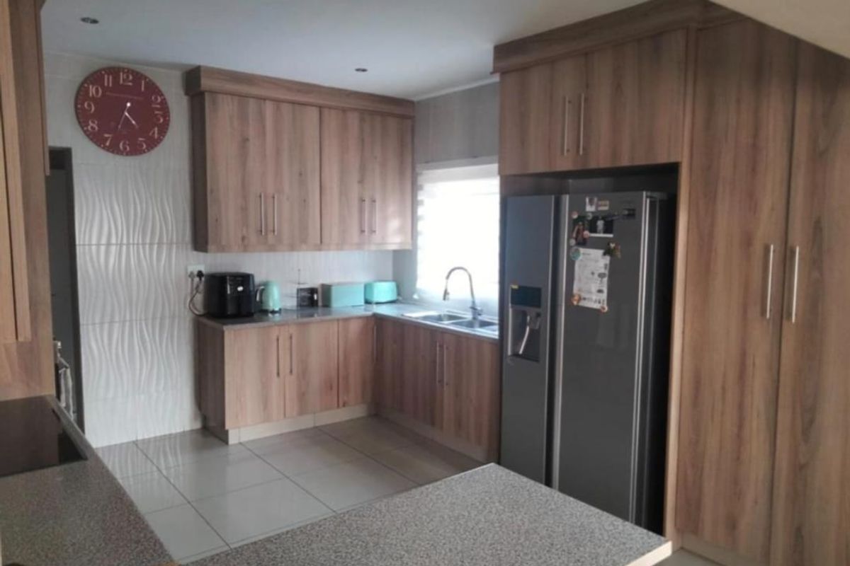 A functional kitchen featuring wood-look cabinetry, tiled flooring, a double sink, and a built-in pantry cupboard.