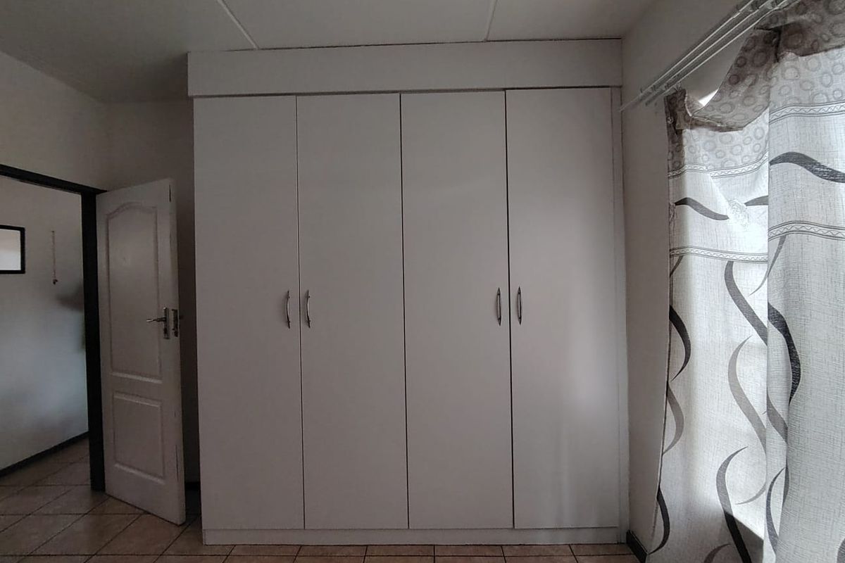 A bedroom featuring built-in white cabinetry, tiled flooring, and a standard interior door leading to the hallway.