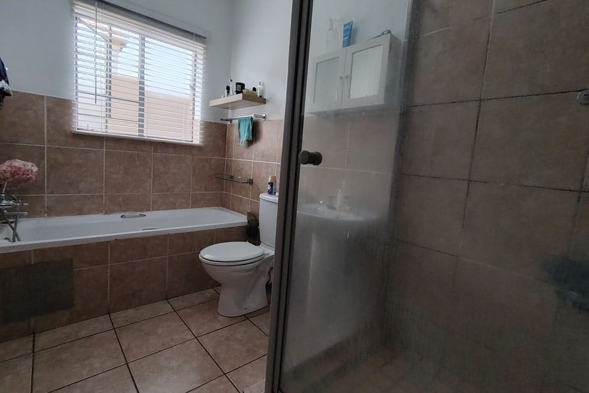 A functional bathroom featuring a tiled bathtub, a separate glass-enclosed shower, a pedestal basin, and a toilet with neutral wall and floor tiling.